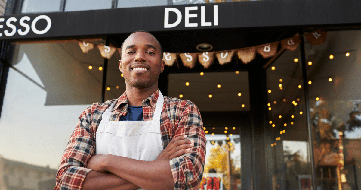 Smiling small business owner in front of deli, showcasing entrepreneurial spirit and success with business lines of credit.