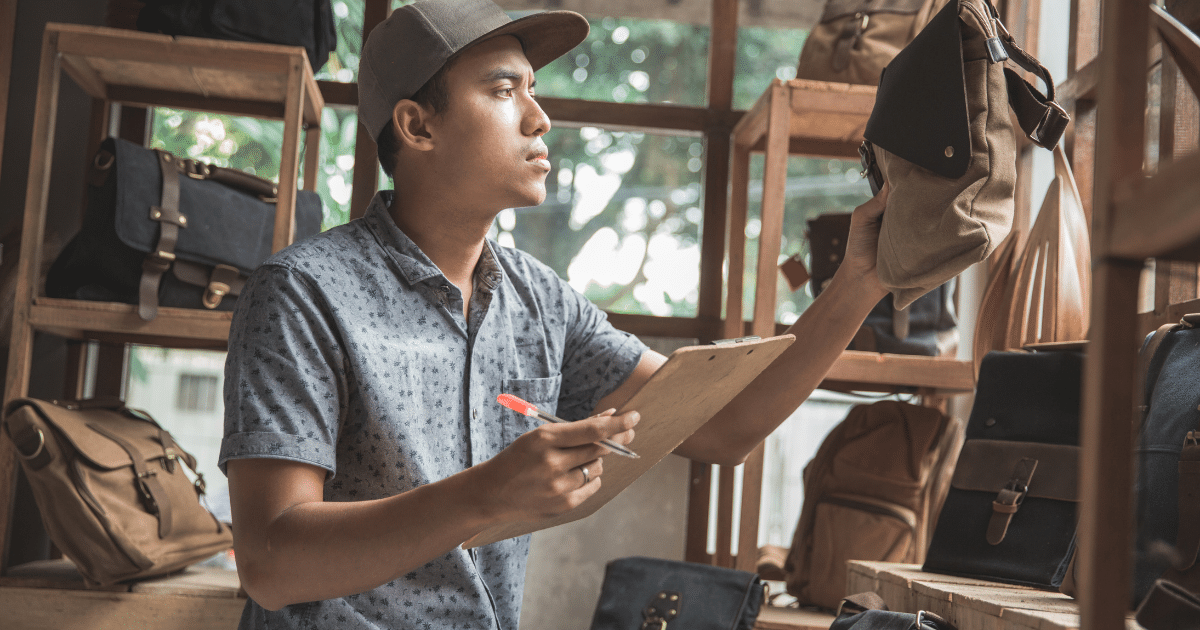 Young man assessing inventory of bags in a retail store, highlighting the importance of business funding and growth opportunities.