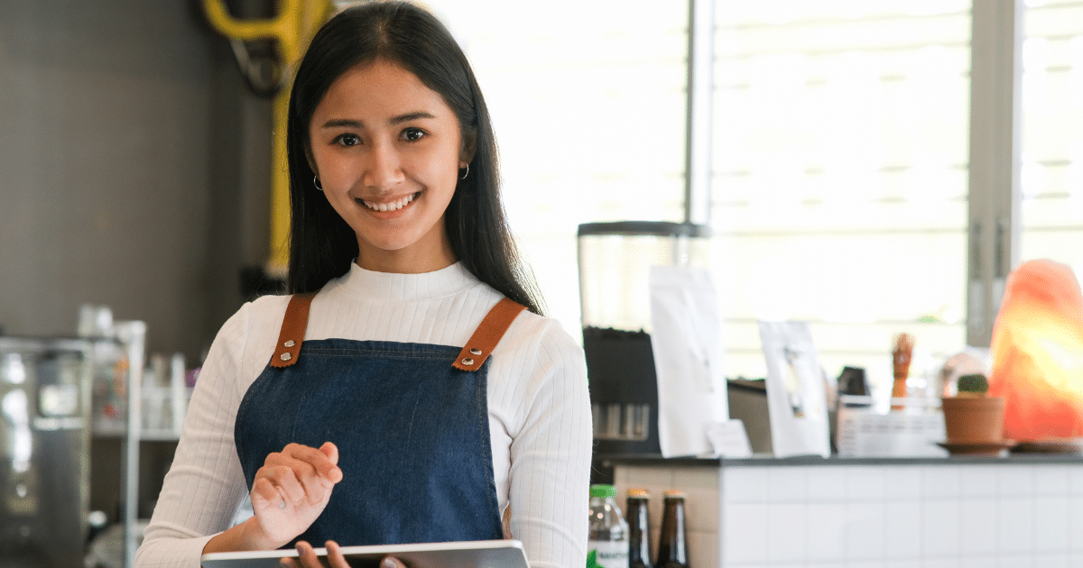 Smiling young woman in a cafe holding a tablet, representing small business growth and profit potential strategies.
