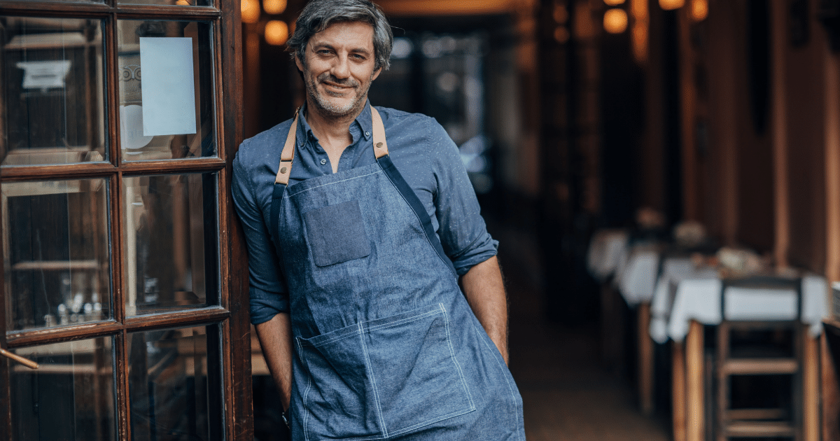 Smiling restaurant owner in apron, showcasing teamwork and leadership in business success and employee empowerment.