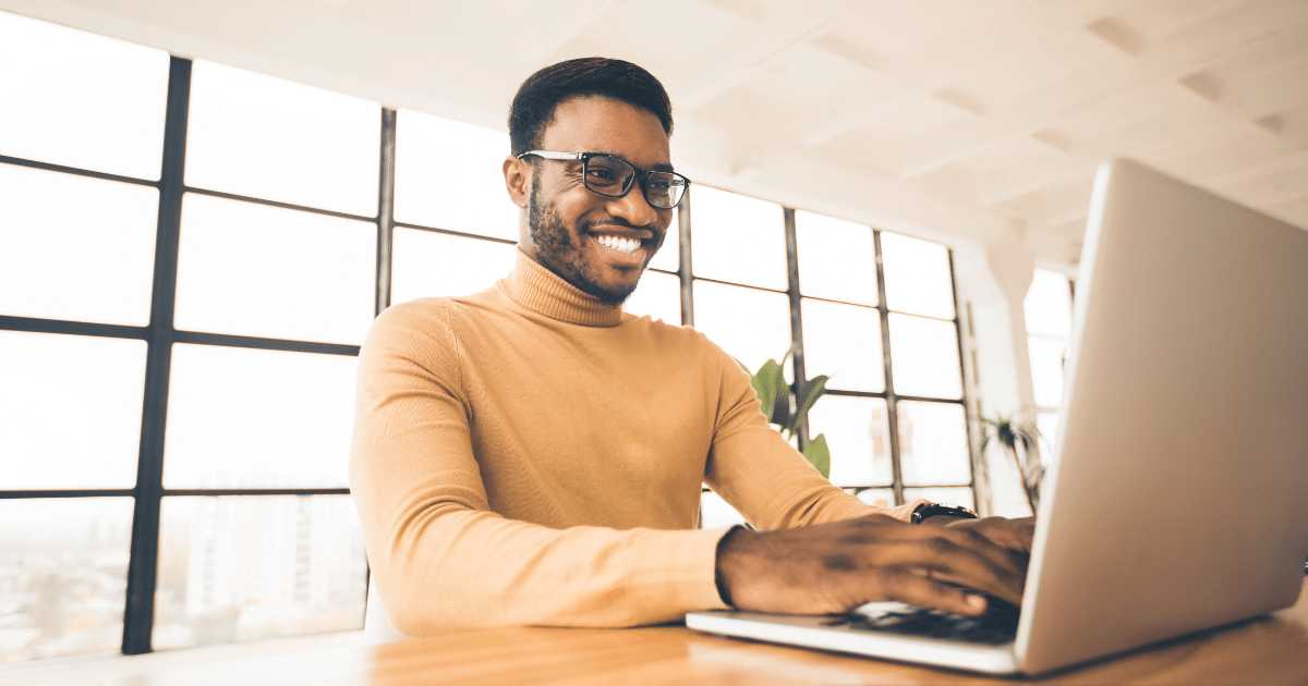 Smiling man in a turtleneck working on a laptop, representing strategies for diversifying customer base.