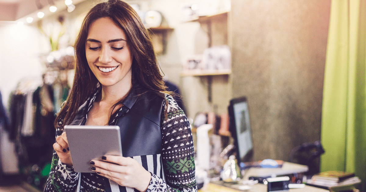 Smiling woman using a tablet in a retail store, exploring holiday loans for small business inventory and staffing needs.