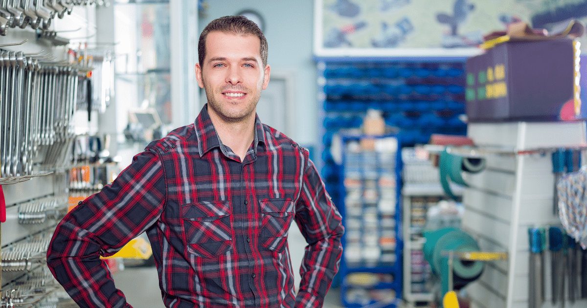 Smiling man in a plaid shirt standing in a manufacturing tools store, representing unsecured loans for manufacturing businesses.