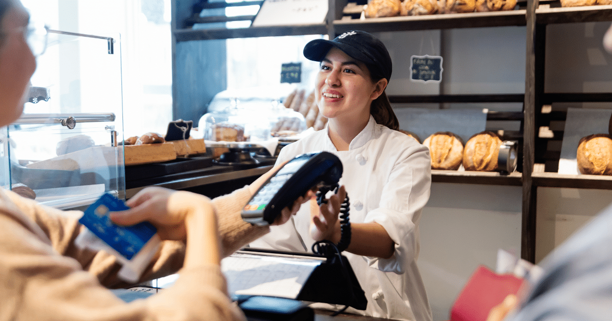 Business financing solutions for growth, featuring a cashier assisting a customer with payment in a bakery setting.