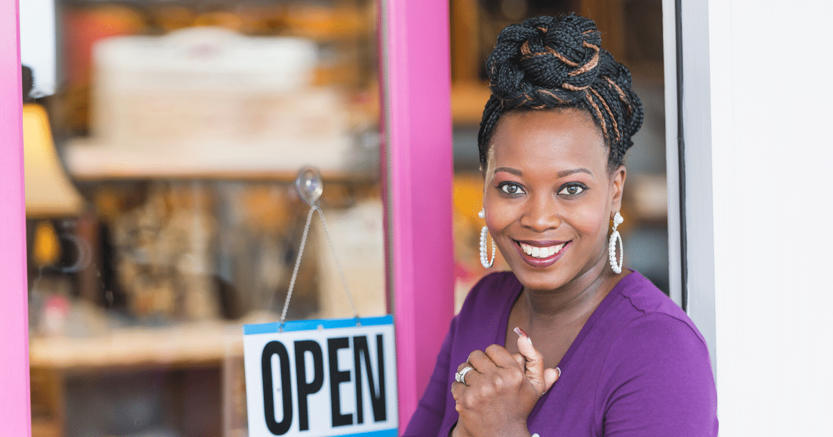 Smiling business owner in front of an open sign, representing small business empowerment and cash advance solutions.