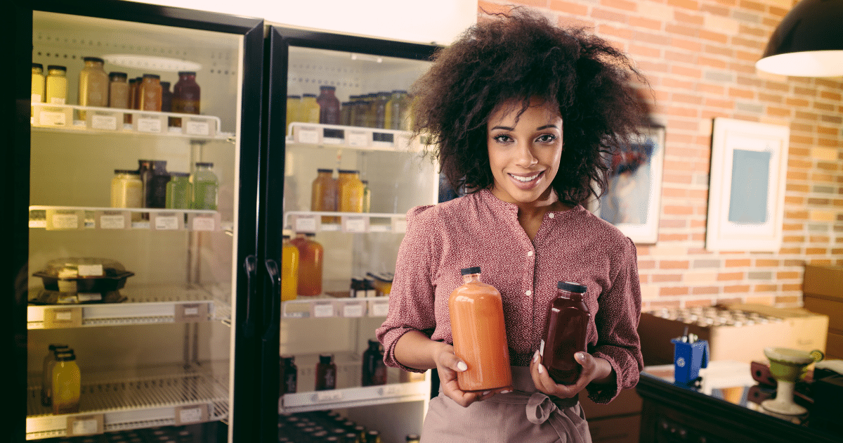 Smiling woman holding juice bottles in a small business, showcasing cost-cutting strategies for entrepreneurs.
