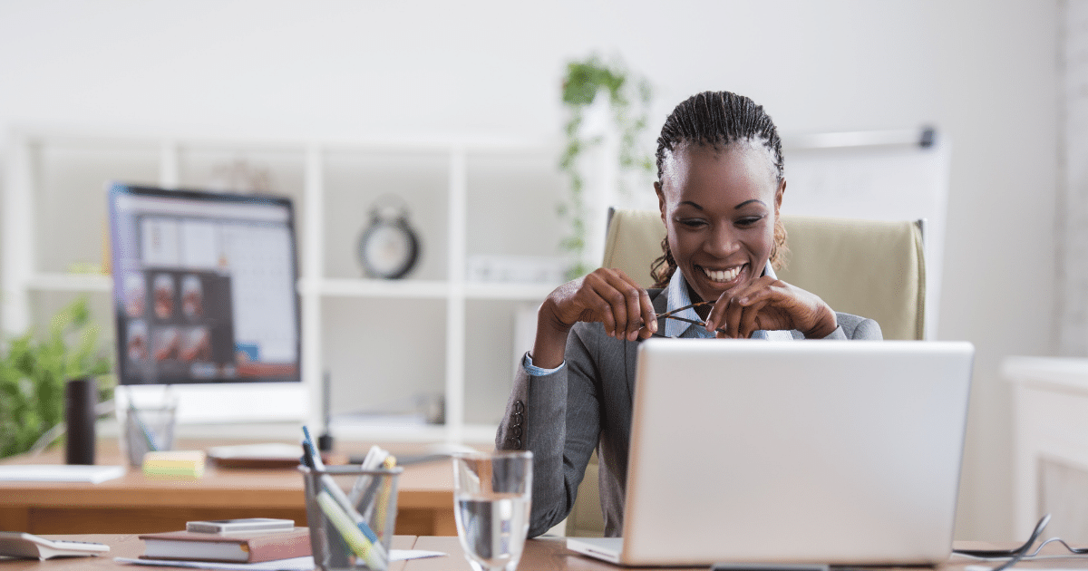 Smiling businesswoman engaging with online marketing strategies at her desk with a laptop and multiple screens.