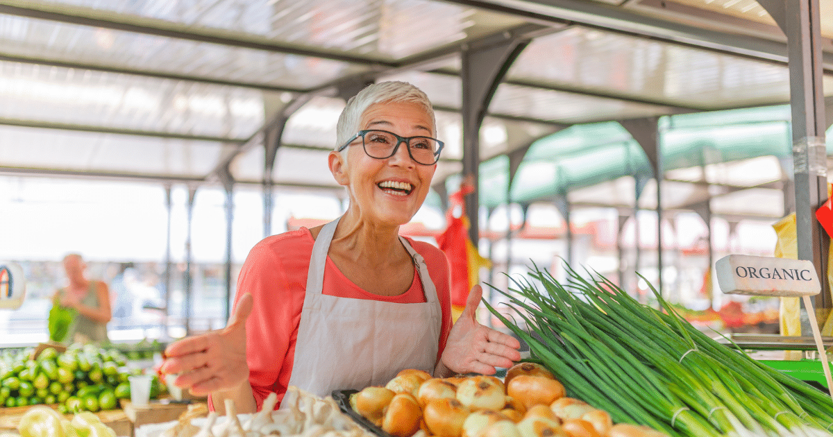 Smiling vendor at a market showcasing fresh organic produce, emphasizing customer service and community engagement.