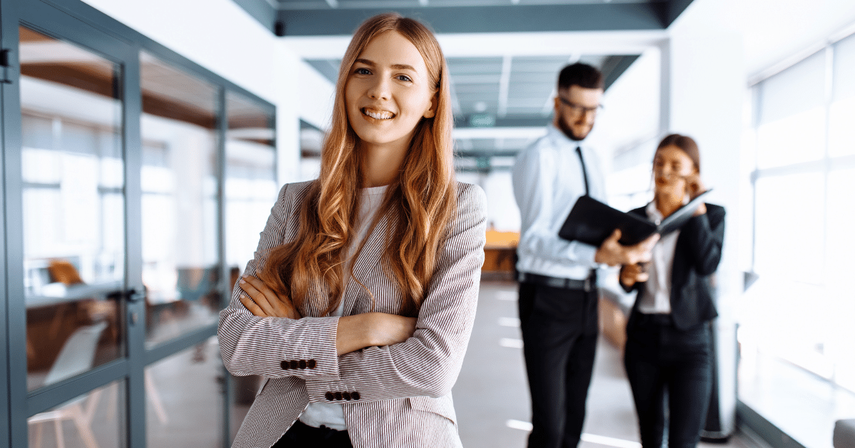 Professional woman smiling confidently in a modern office, showcasing business efficiency and teamwork with colleagues.