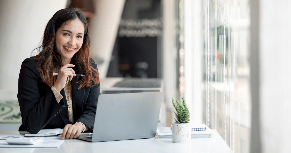 Professional woman smiling at a desk with a laptop, pen, and office supplies, representing affordable office equipment upgrades.