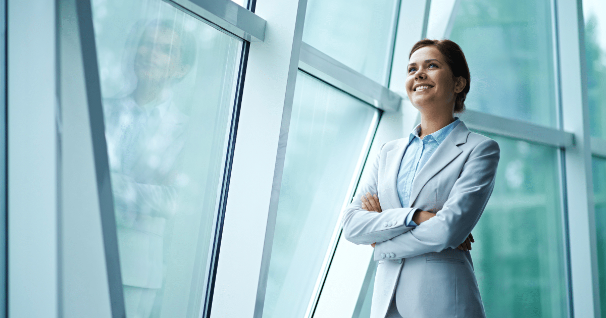 Business professional smiling by large windows, promoting office energy efficiency and savings strategies.