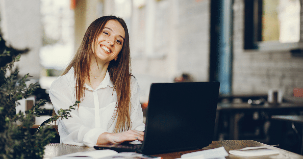 Smiling woman working on a laptop in a cafe, representing social media branding strategies for businesses.