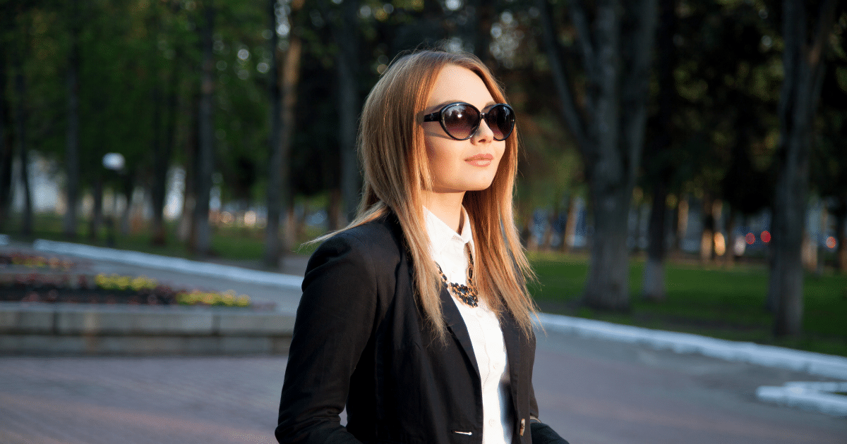 Business professional in sunglasses, exuding confidence and style in a park setting, representing success strategies.