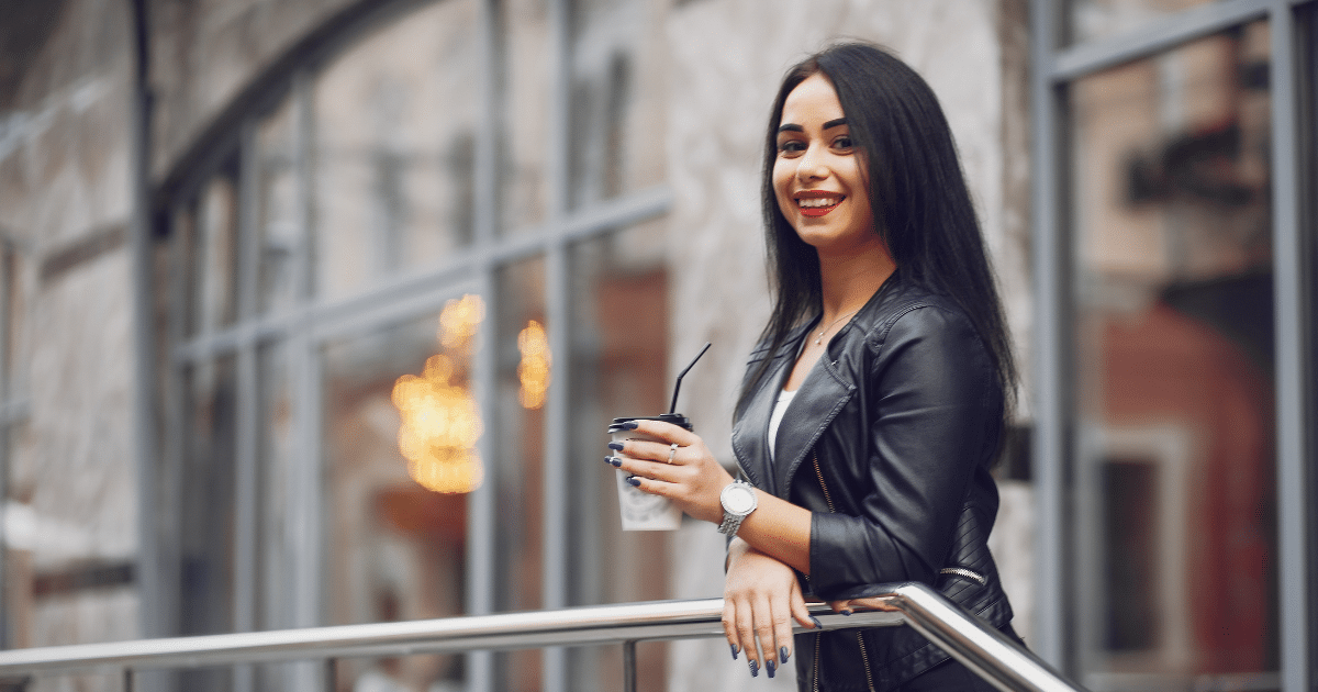 Smiling woman in a leather jacket holding a drink, representing customer engagement and inviting business atmosphere.