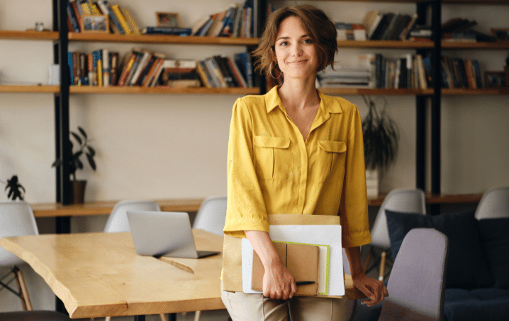 Businesswoman in a yellow shirt holding documents, representing financial empowerment and avoiding personal savings for business expenses.