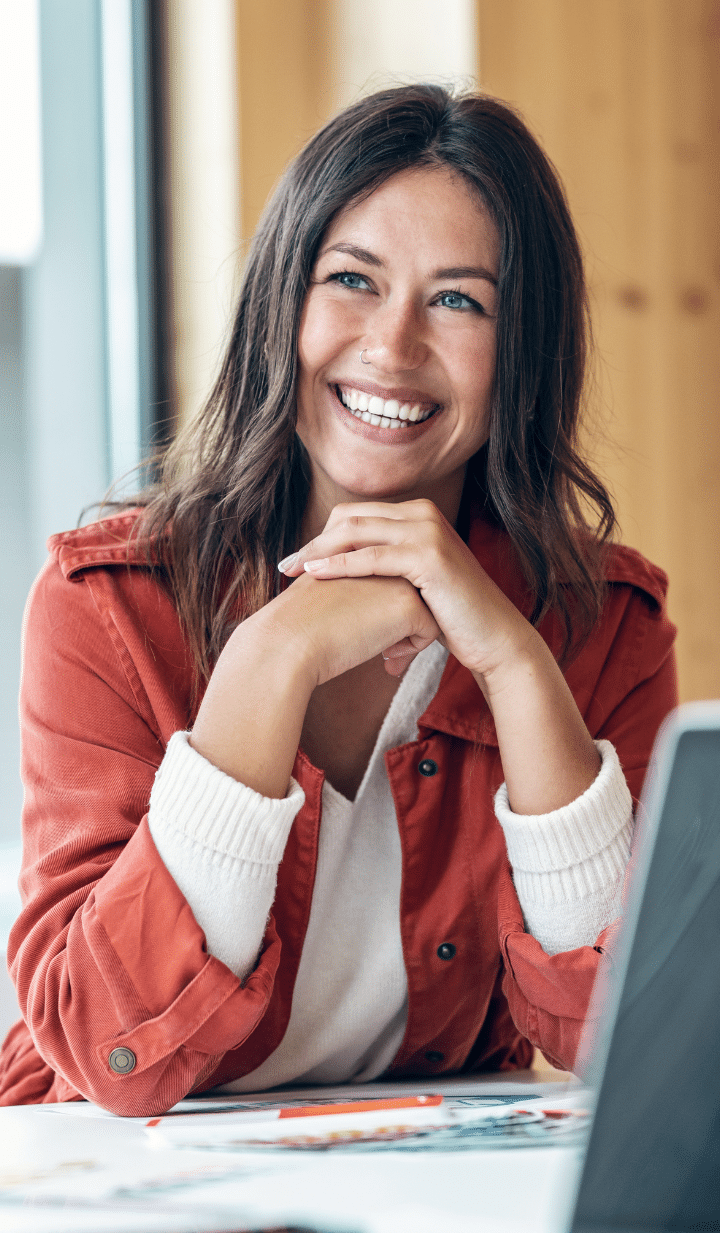 Smiling woman in a red jacket at a desk, representing fast and flexible business loan solutions.
