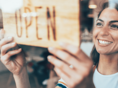 Smiling woman hanging an 'OPEN' sign, representing small business recovery and unsecured credit lines after Hurricane Sandy.