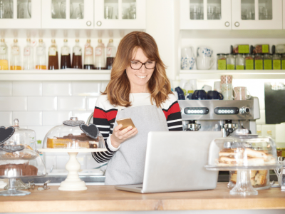 Woman in a cafe using a smartphone and laptop, exploring unsecured investment opportunities with social capital.