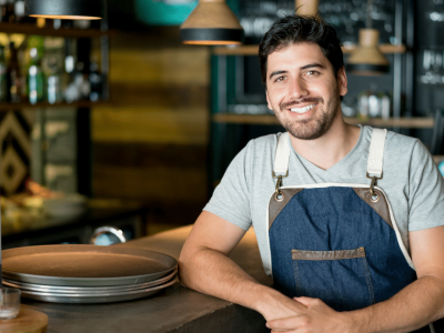 Smiling restaurant owner in apron at a busy bar, showcasing business growth and cash flow solutions for seasonal success.