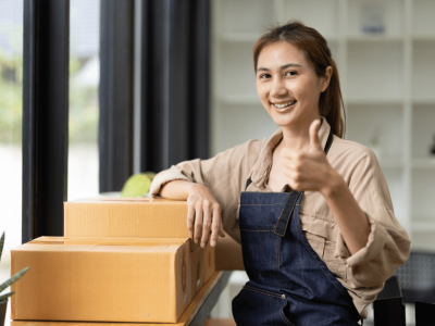 Smiling woman giving a thumbs up next to boxes, representing growth in pharmacy and medical equipment businesses.