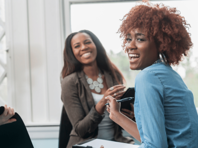 Two women smiling and engaging in a discussion, representing teamwork and support in financial recovery and credit repair strategies.