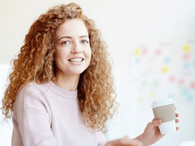 Smiling woman enjoying coffee in a workspace, representing effective stress relief techniques for busy workdays.