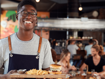 Smiling restaurant server holding a burger and fries, showcasing restaurant dining experience and financing opportunities.