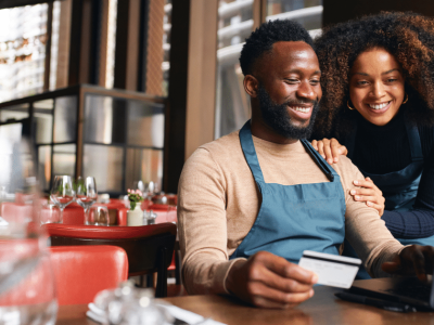 Restaurant owners exploring financing options while using a laptop and credit card in a vibrant dining setting.